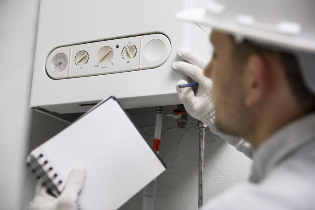 Worker wearing a white hat and holding a note pad looking at white hot water heater.