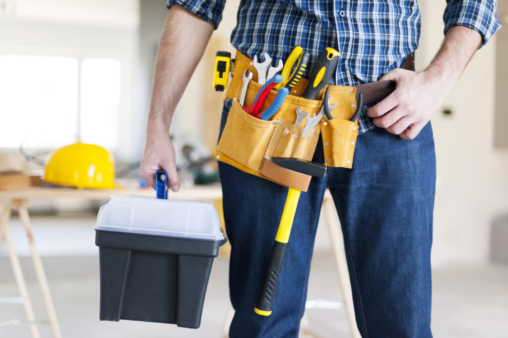 Male construction worker wearing yellow tool belt and carrying a box