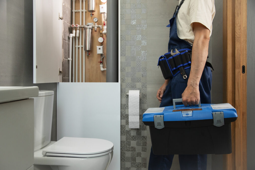 Male plumber carrying toolbox walking over to a toilet and water heater